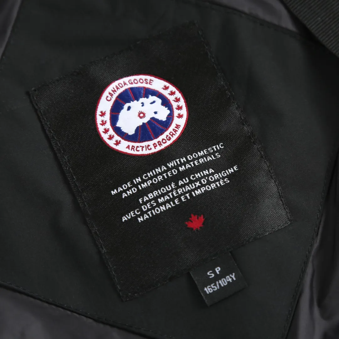 P1060 Canada Goose hooded down jacket fabric selection; nylon fabric is known for its high strength, excellent wear and tear resistance, and excellent durability. At the same time, it is light in texture, easy to move, and has excellent water-repellent function, which can effectively deal with light rain and humidity. Technology: Double-needle quilting technology is used. Double-needle quilting technology is a sophisticated sewing technology. Its core feature is to use two needles to quilt at the same time to form two parallel stitches. This design not only makes the quilting lines visually more three-dimensional, regular and refined, but more importantly, it greatly enhances the firmness of the sewing. The double lines in parallel form a more stable structure, which can effectively lock the internal filling and significantly prevent it from shifting, accumulating or velveting during wearing or washing, thereby ensuring that the thermal insulation layer is evenly distributed without cold spots, and comprehensively improves the durability and thermal efficiency of the product.    High-quality filling: It is filled with 90% selected white duck down, weighing 170g, ensuring fluffy rebound, lightness and warmth.  Accessories: one-to-one customized three-standard, one-to-one customized zipper, one-to-one customized hardware
